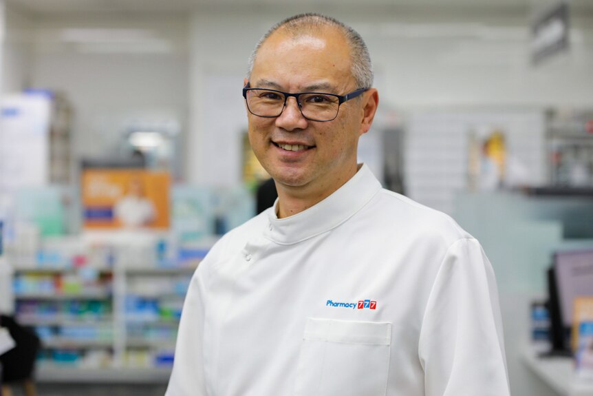Andrew Ngeow standing in a pharmacy wearing a white pharmacist's uniform.