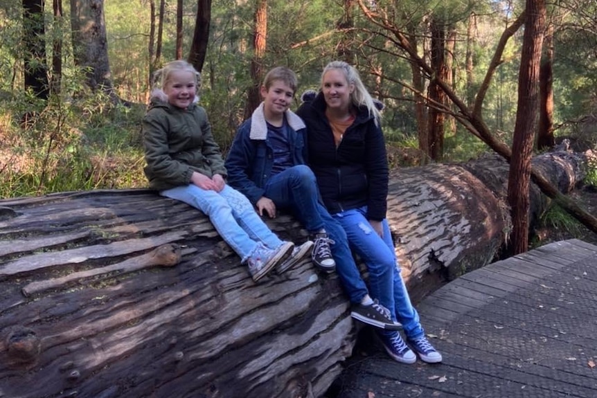 Melissa, Aubree and Jacob sitting on a log in the bush and smiling for a photo 