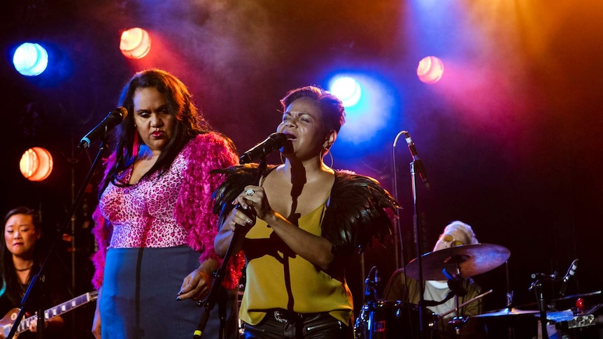 Elaine Crombie (left) and Ursula Yovich (right) singing on stage with a guitarist and drummer in the background.