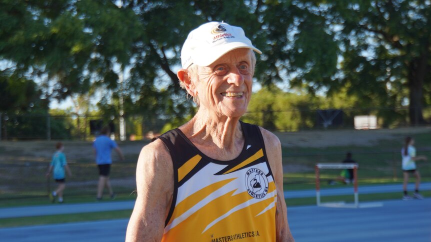 An elderly gentleman smiles at a friend. he's wearing a hat and a yellow running shirt.