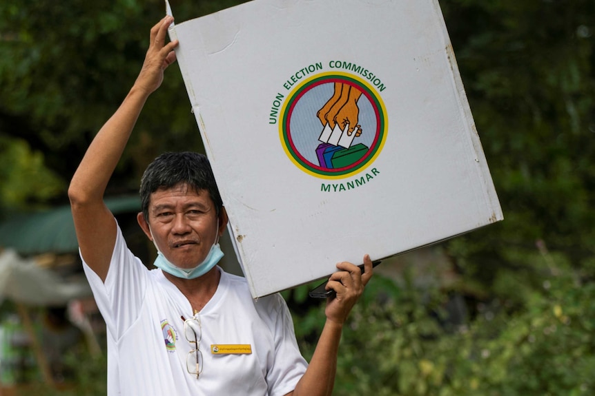 A person with a mask around his chin carries a Myanmar ballot box.