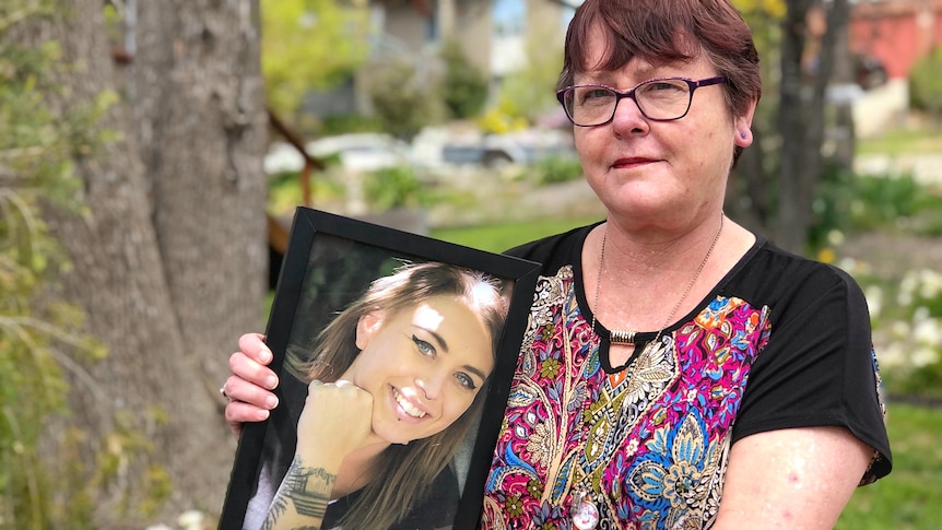 A woman holds a framed picture of her daughter.