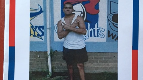 Aboriginal man stands in front of wall with arms crossed