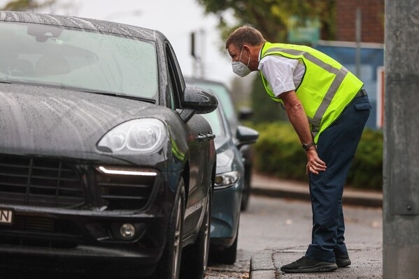 An official in a high-vis vest leans down to talk to a driver through the passenger-side car window.