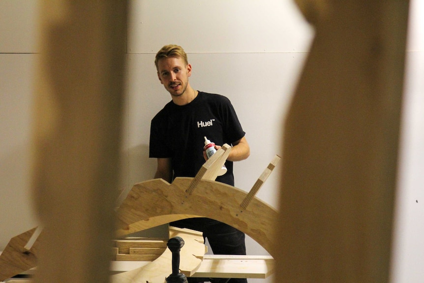 Thomas Wing-Evans between two of the wooden structures, with glue in his hand.