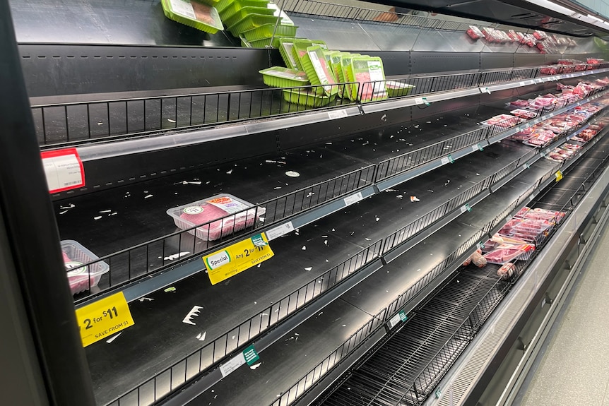 Rows or empty or near-empty shelves in the meat section at a supermarket.