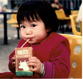 A young girl drinks milk out of a box that has Chinese writing and packaging.