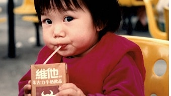 A young girl drinks milk out of a box that has Chinese writing and packaging.