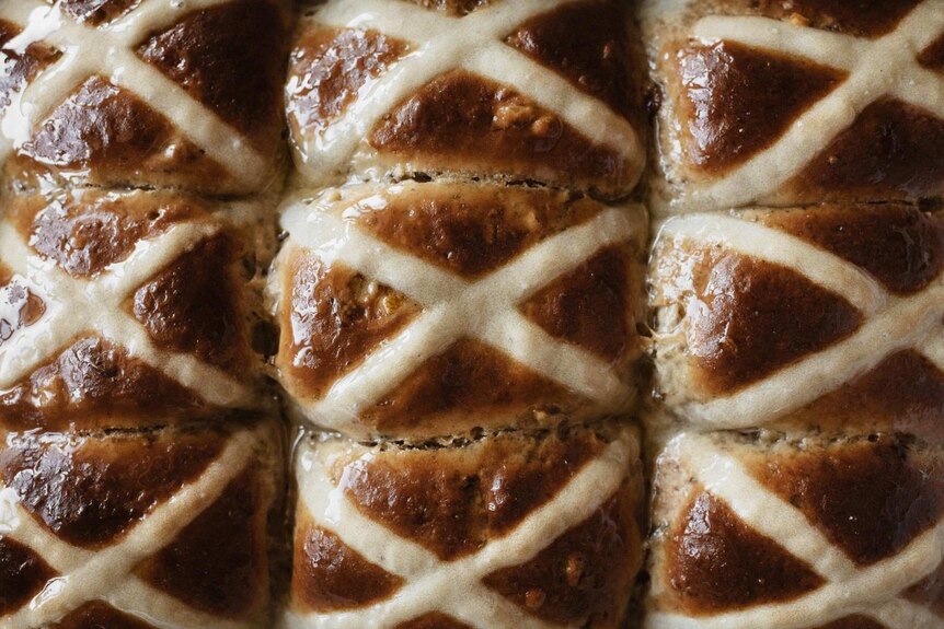 A close up of six hot cross buns that have been glazed, ready for Easter spent at home.