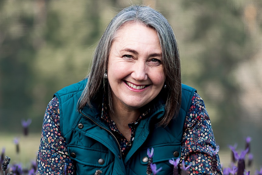 woman smiling while leaning over a row of flowering plants