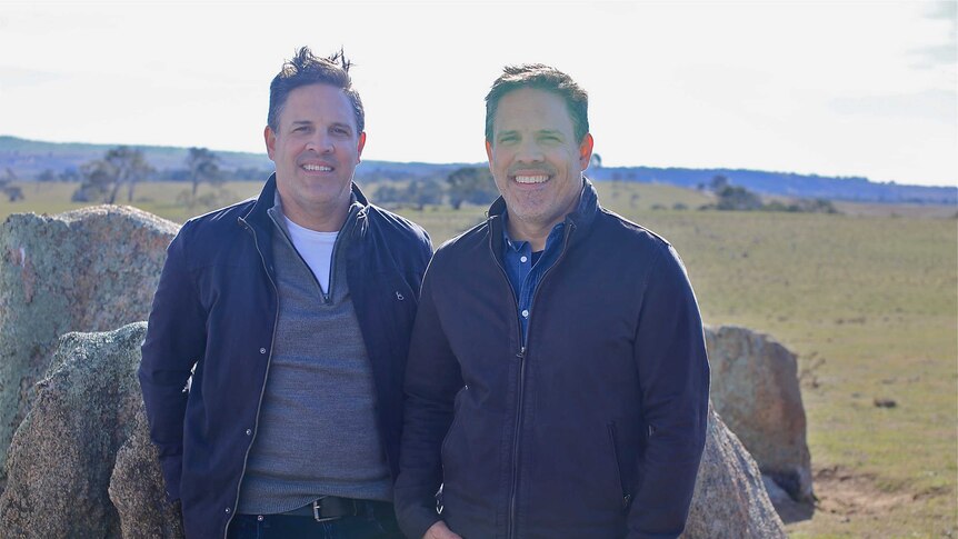 Two identical twins standing side by side in a field out in NSW