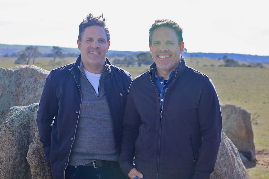 Two identical twins standing side by side in a field out in NSW