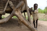 A thin child in South Sudan stands next to his family's grain store.