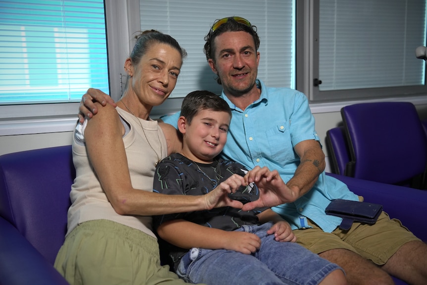 A woman, man and young boy sit smiling on a couch with their arms around each other