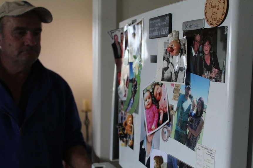 A man looks solemnly at his fridge filled with family photos.