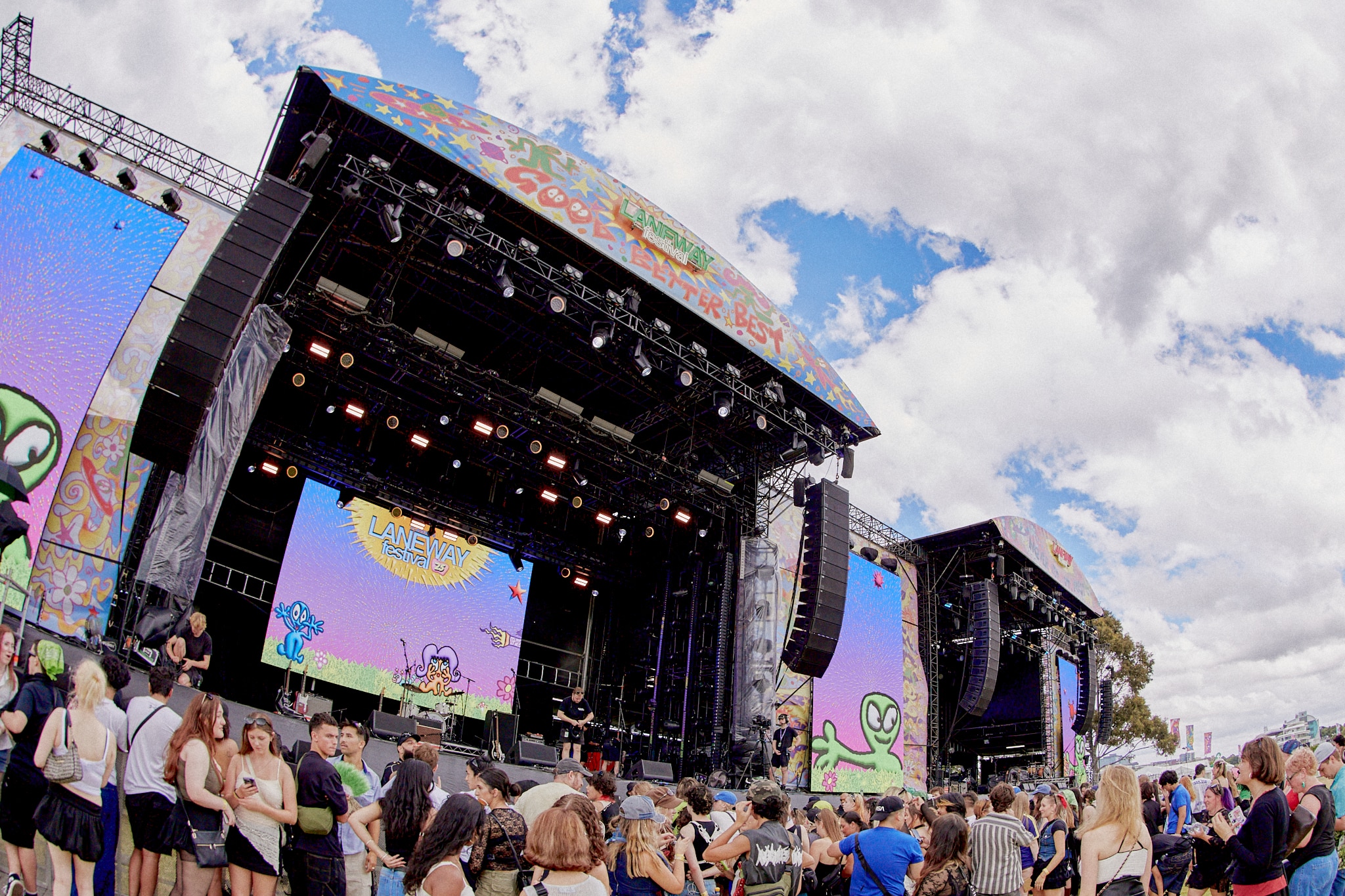 Vibrant crowd at Laneway Festival stage with colorful lights and performers in the foreground, capturing the energetic atmosphere of live music discovery.