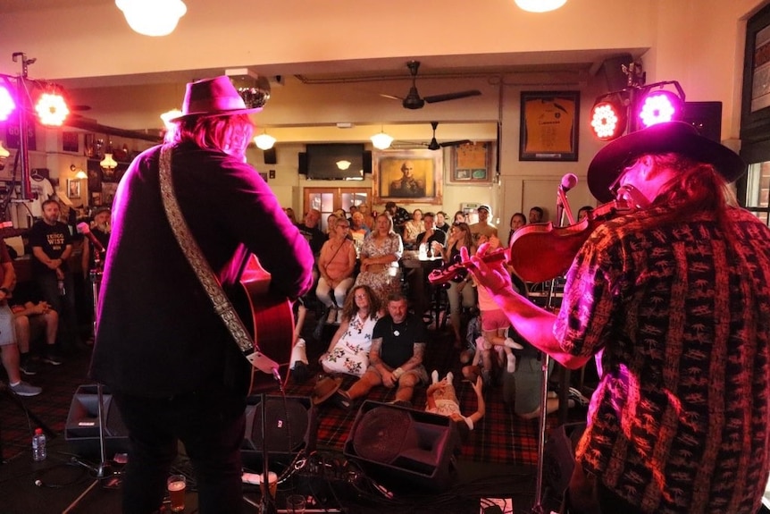 Two men performing on stage in a country pub — one playing a guitar and the other a violin.