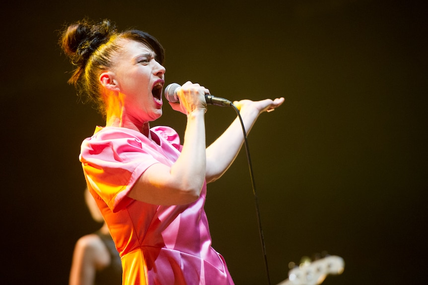 Kathleen Hanna screams into the microphone with her left arm out-stretched