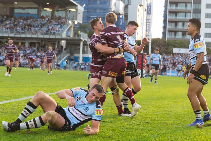 Manly players hug in celebration while despondent Sharks players hang their heads or lay on the ground.