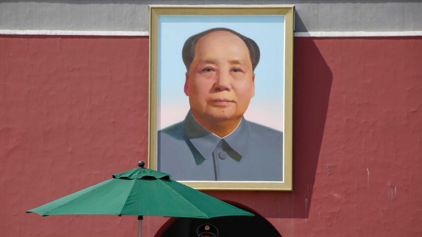 A policeman stands in front of a portrait of Mao Zedong.
