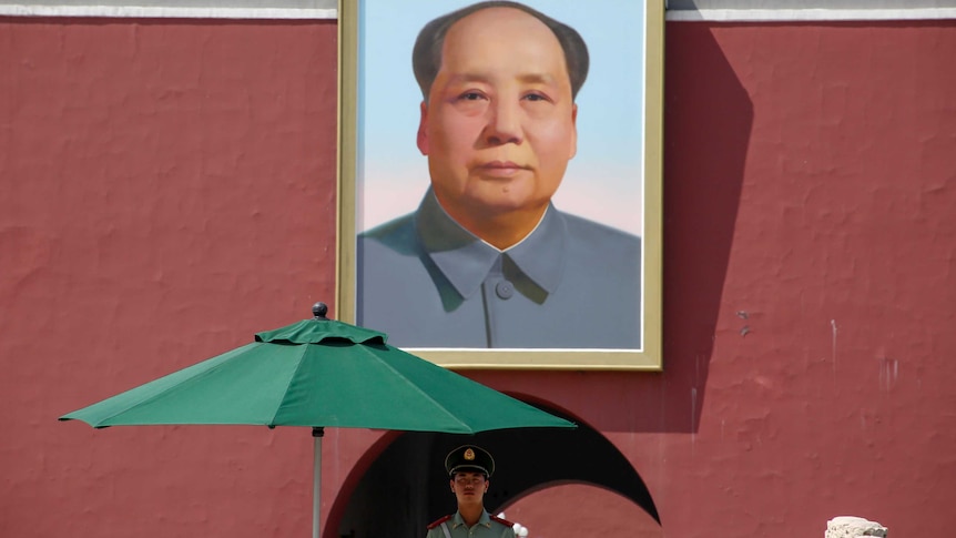 A policeman stands in front of a portrait of Mao Zedong.