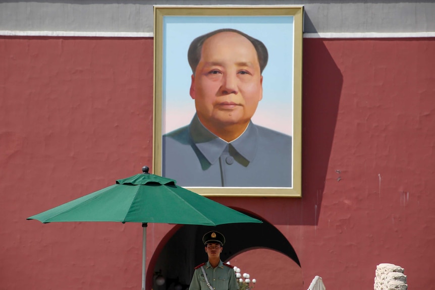 A policeman stands in front of a portrait of Mao Zedong.