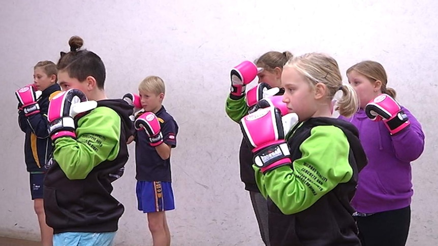 A group of primary school aged children stand at the ready wearing bright pink boxing gloves.