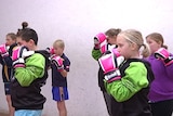 A group of primary school aged children stand at the ready wearing bright pink boxing gloves.