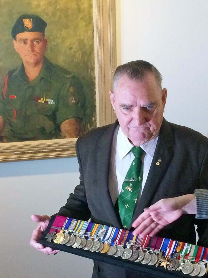Keith Payne VC standing with his portrait and medals at the Australian War Memorial.