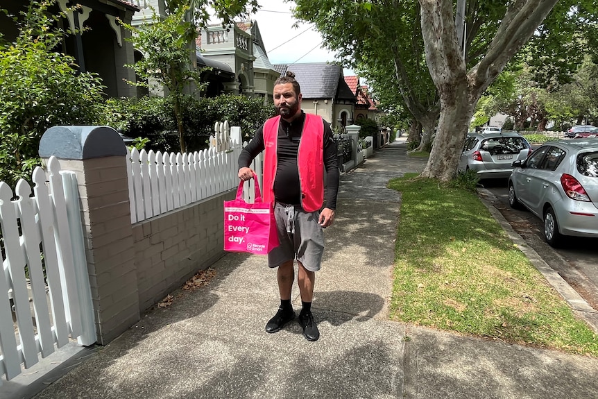 A man wearing a pink vest and carrying a pink bag in a street in Sydney.