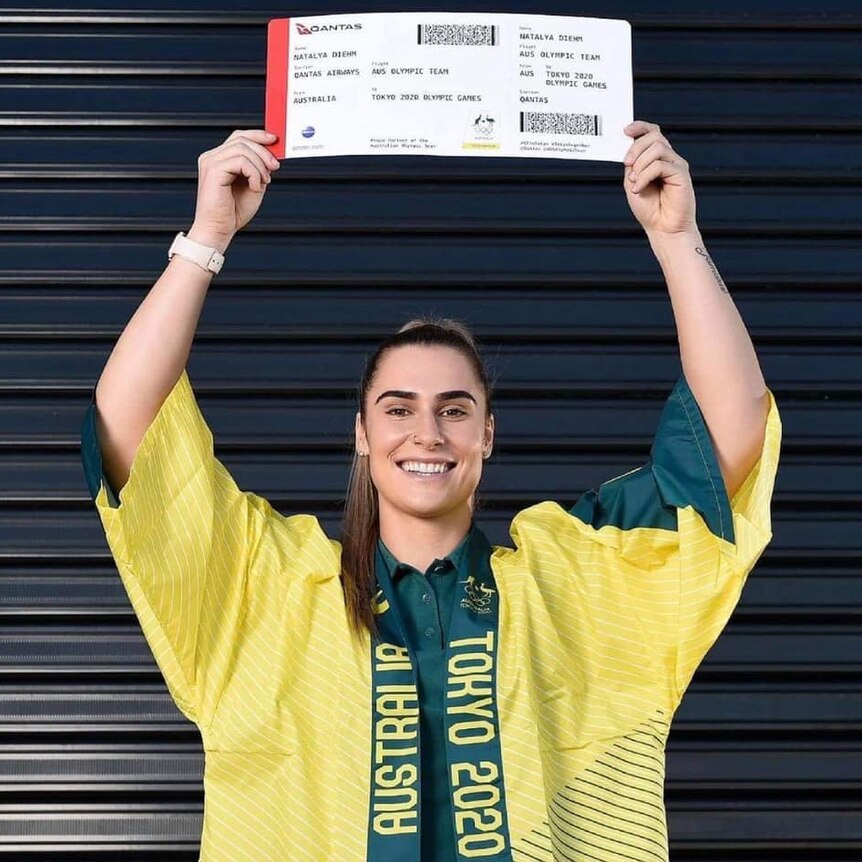 A woman in a green and gold robe holds up a large boarding pass - her ticket to Tokyo.