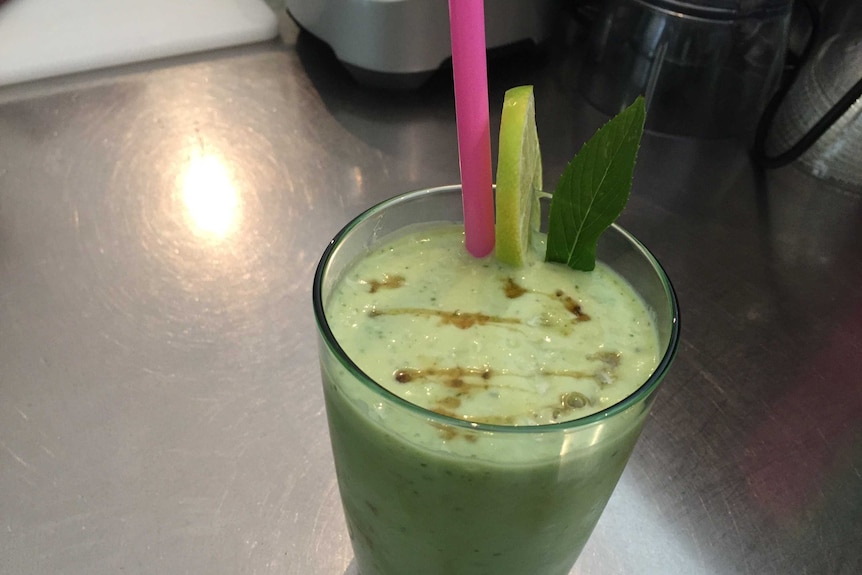 Glass of green blended avocado with straw and mint leaf