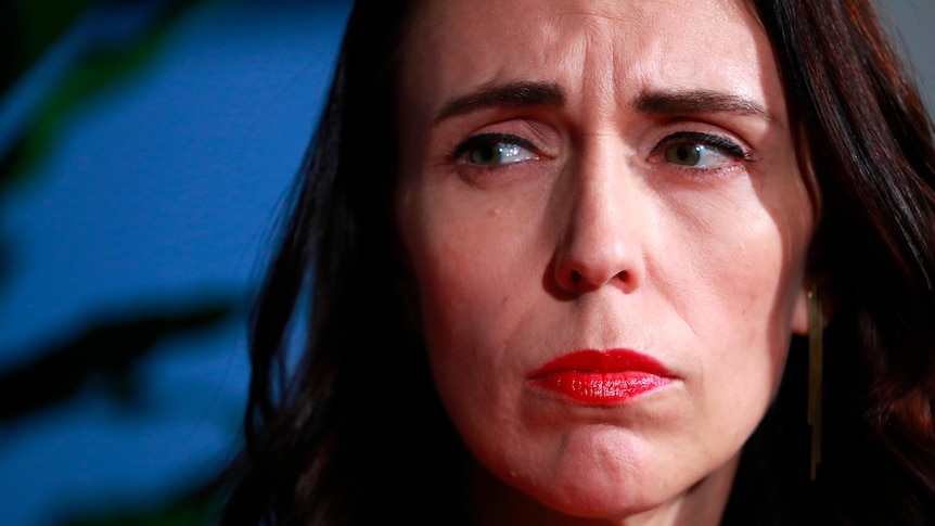 Jacinda Ardern with a bold rep lip looking sombre 