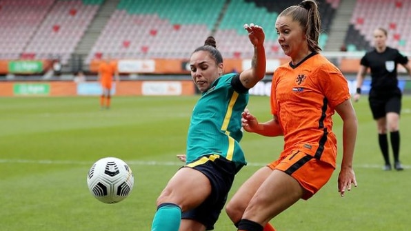 Female soccer players chasing down a ball with the opposition player behind her as they race for the ball during a match