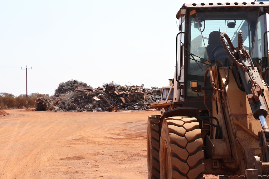 A yellow digger in front of a pile of metal recycling. 