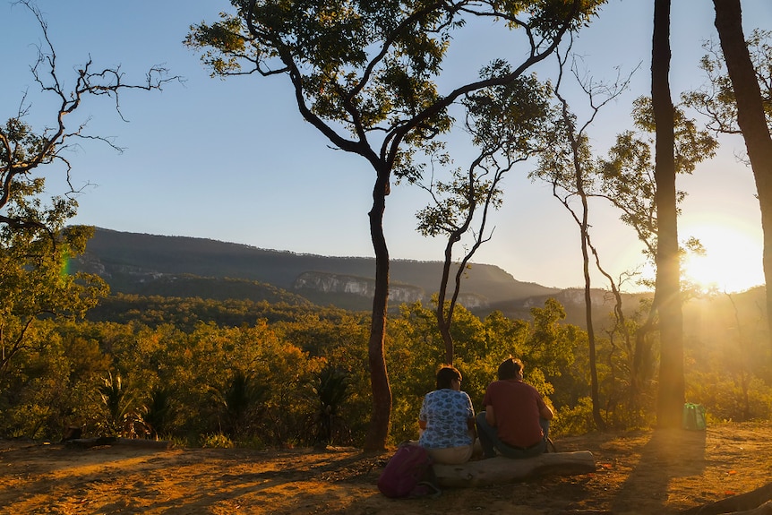 Two people sit on a log watching the sunset over Carnarvon Gorge.