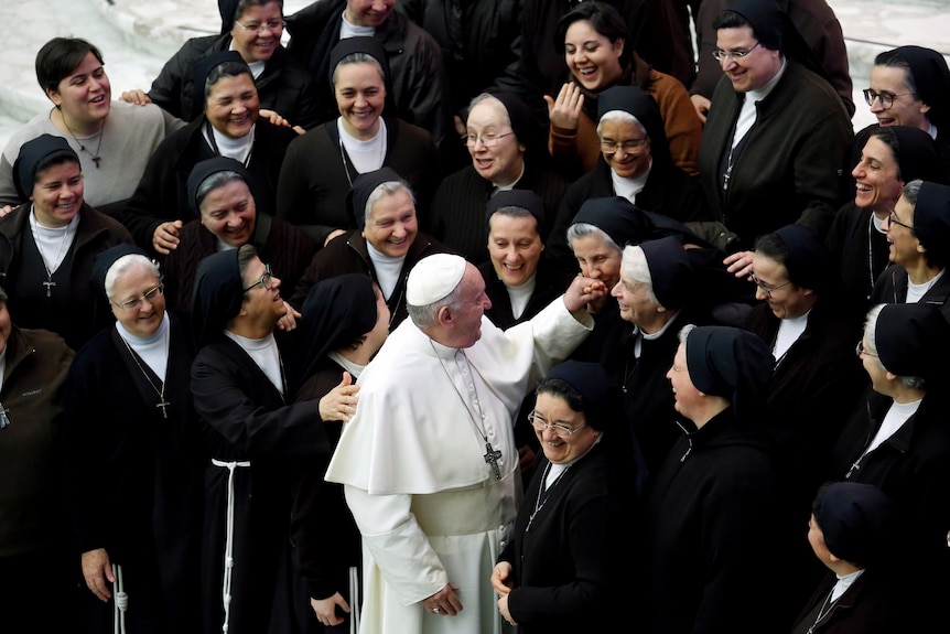 Pope Francis smiles at a nun who kisses his hand among a crowd of nuns