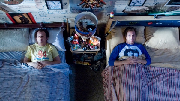 Two adult men sleep in separate beds opposite each other