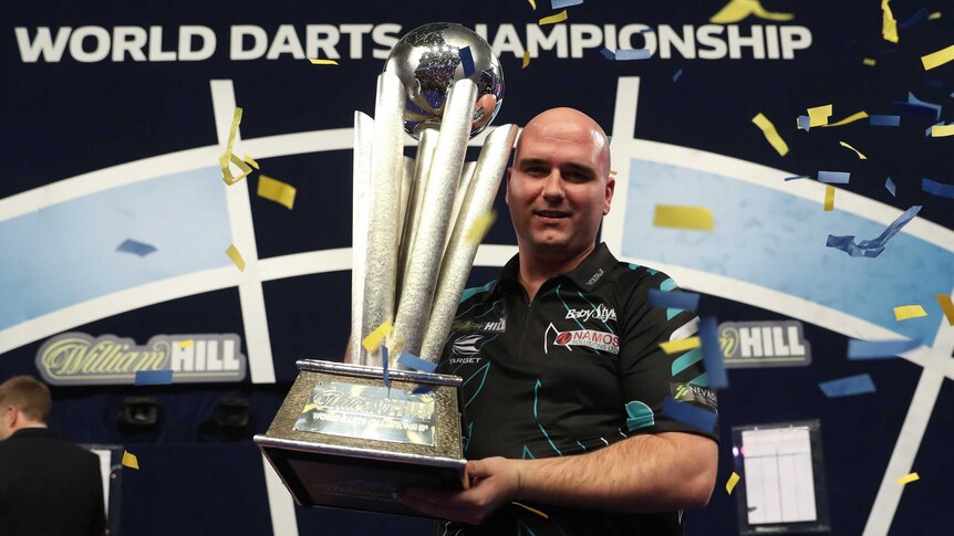 Rob Cross holds up the world championship trophy with confetti falling around him