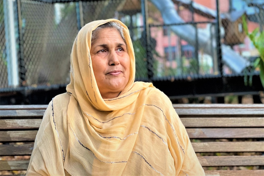 A woman wearing a head scarf sitting on a bench in a park