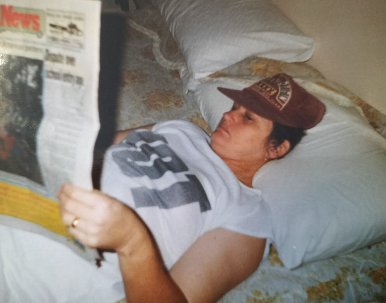 An old photo of a woman lying in a bed, reading a newspaper.