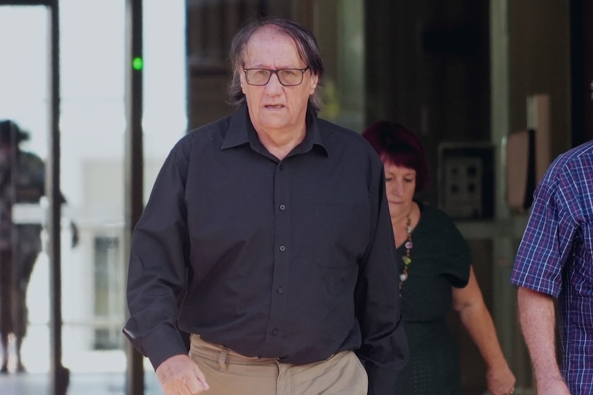 A man in his 60s with long hair, wearing glasses walks out of court.
