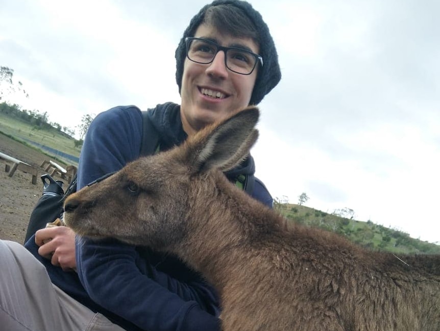 A teenager wearing glasses pats a kangaroo.