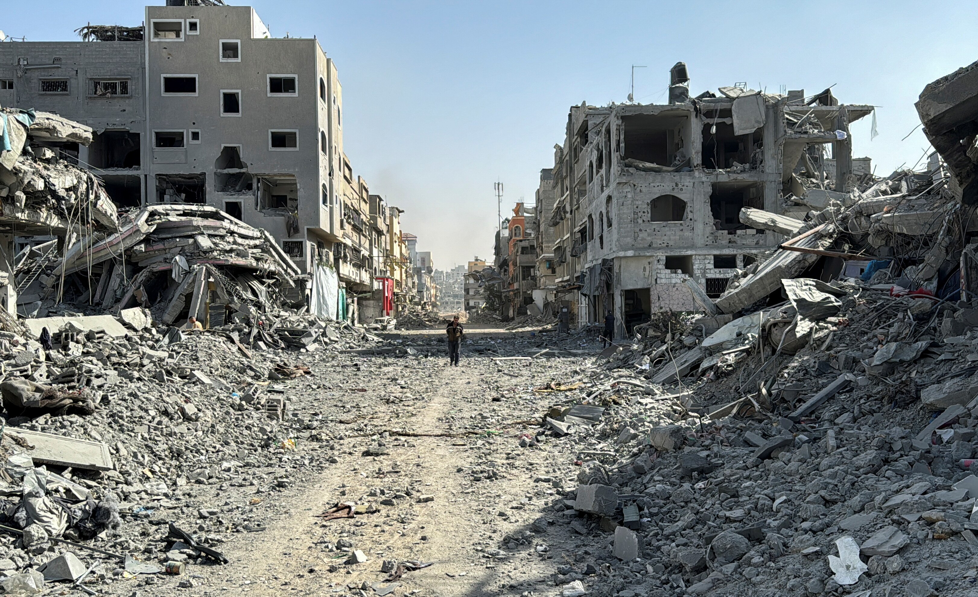 A Palestinian man walks past the rubble of buildings on a street.