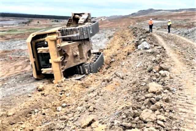 Two people in high-vis clothing standing at a mine site next to heavy machinery that's rolled