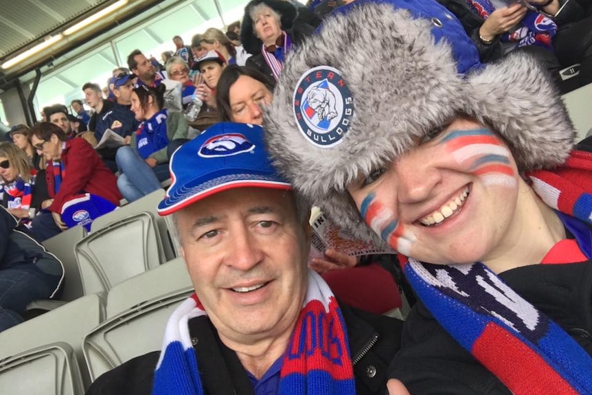 A man and his daughter wearing football team colours sitting in the grandstand.  