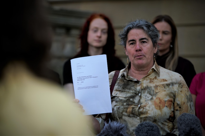 Robin Banks stands in front of two other women, and holds up a piece of paper