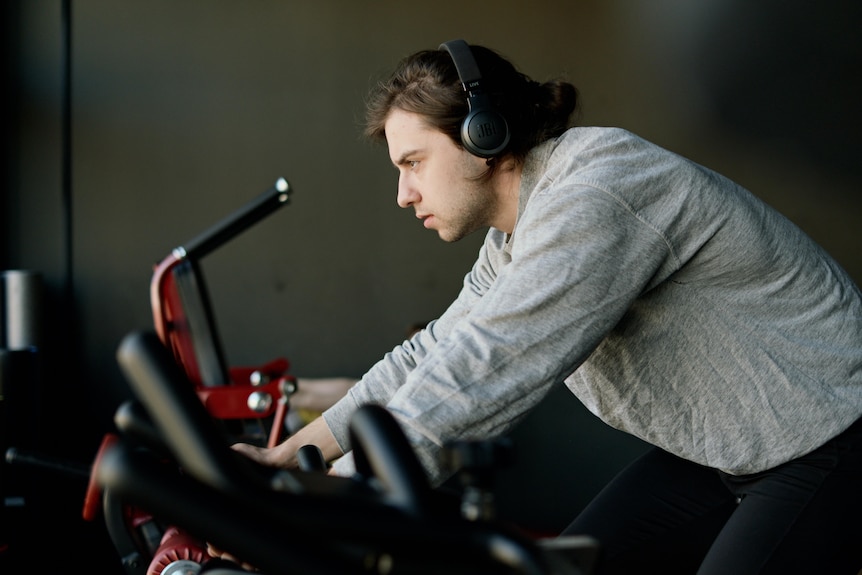 Mężczyzna w słuchawkach pochyla się podczas jazdy na rowerze treningowym
