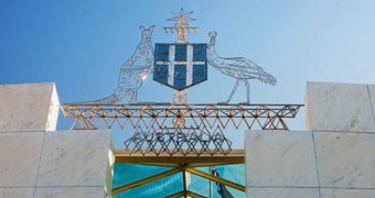 The Australian coat of arms is shown in front of a blue sky.