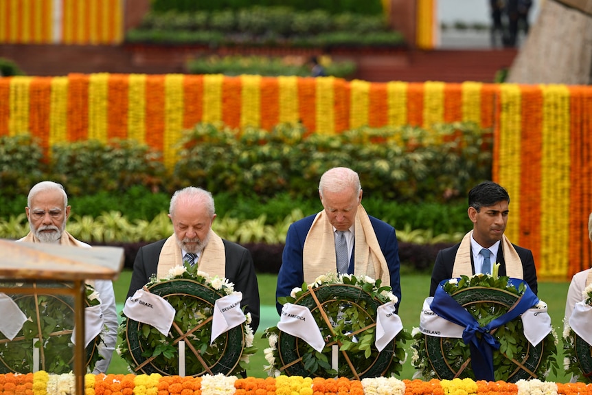 Four men stand in a row at a memorial.